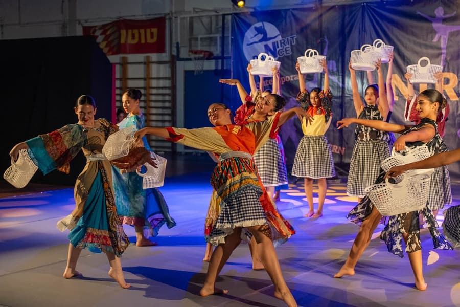 רקדנית בכתום פורשת יד קדימה בריקוד קבוצתי